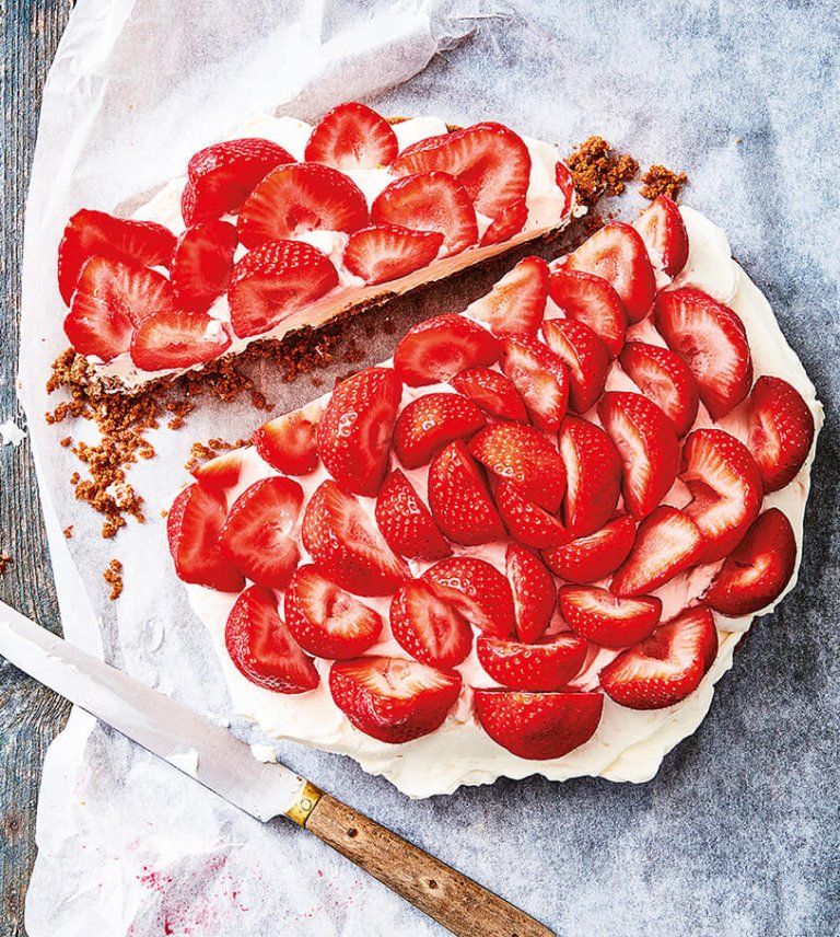 Strawberry-topped cream cake with a crumb crust and sliced fresh strawberries, served on parchment paper with a cake knife beside it.