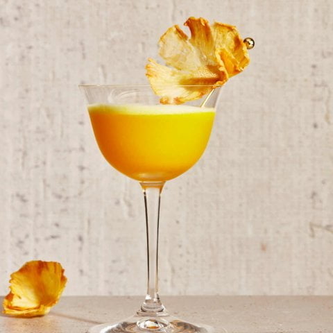 A bright orange cocktail with a pineapple garnish.