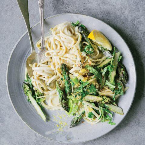 A plate of pasta and asparagus with cutlery.