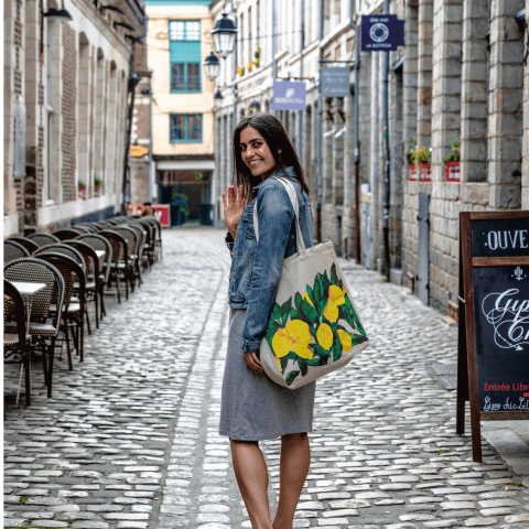 A young woman, Hannah Sunderani, waves to the camera on a cobblestone street.