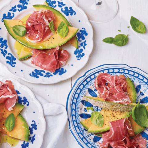 Beautiful overhead image of prosciutto and melon appetizer on blue and white plates