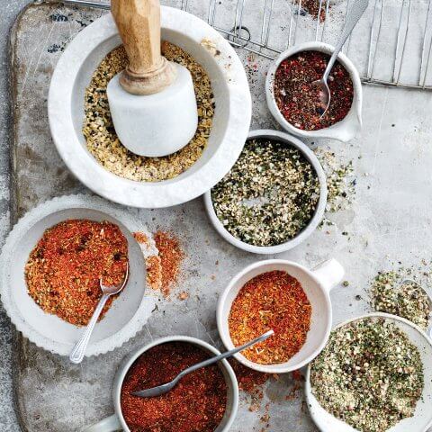 Bowls of mixed spices next to a white mortar and pestle