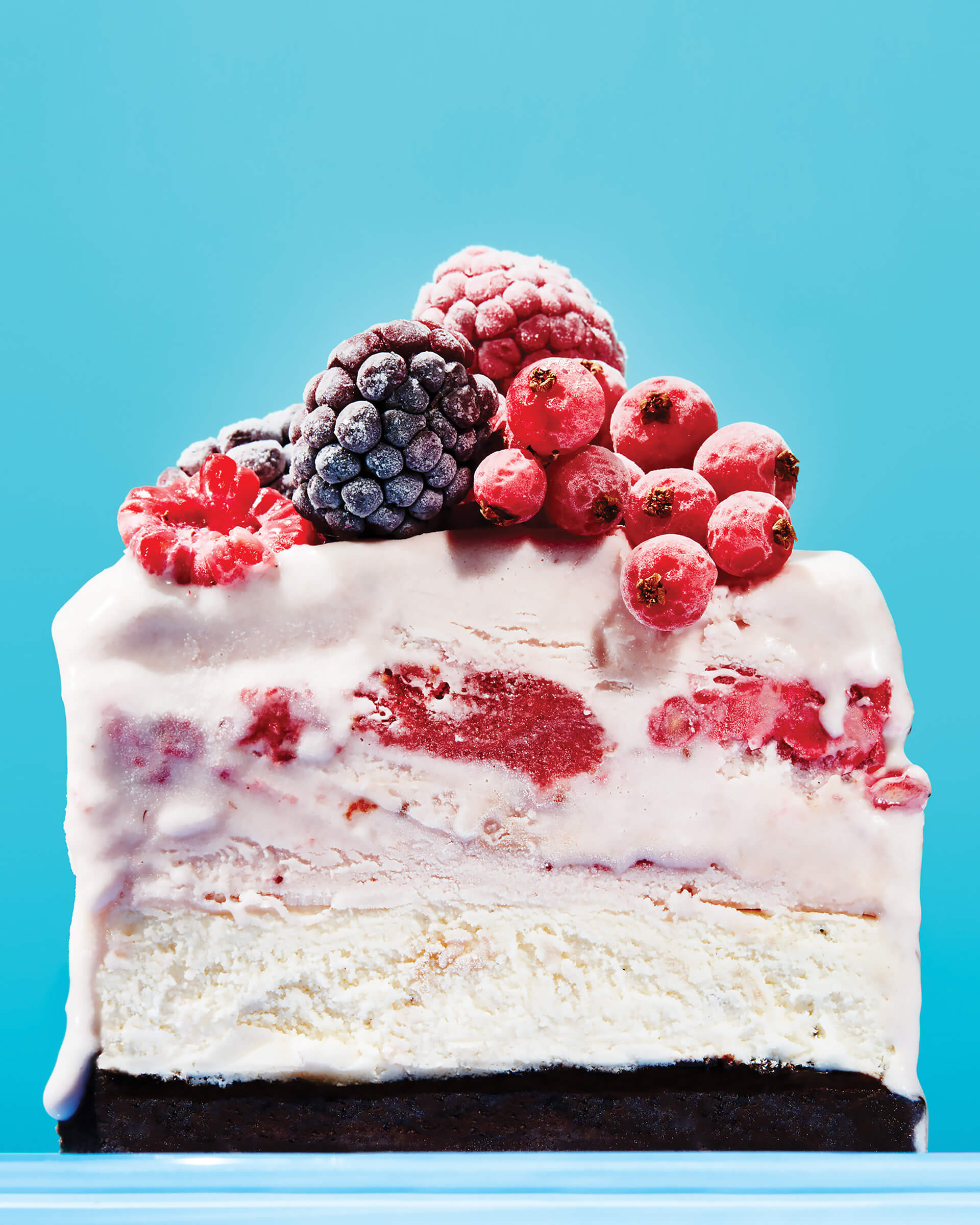 A vanilla ice cream cake with mixed berries against a bright blue backdrop.