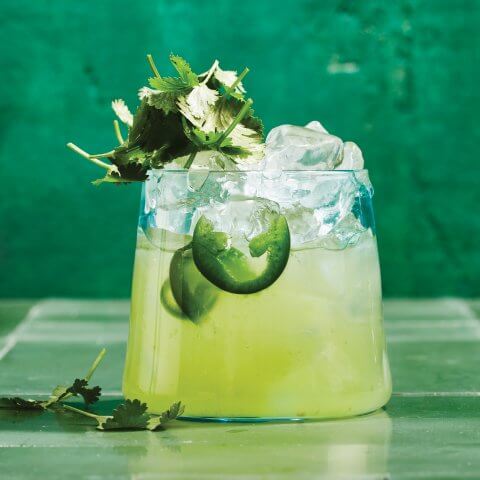 A short glass of limeade against a green backdrop.