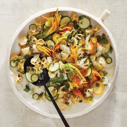A bowl of salad with a black spoon sits on a table.