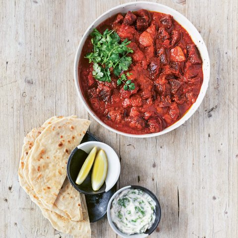 A bowl of curry with bread, lemons and dip on the side