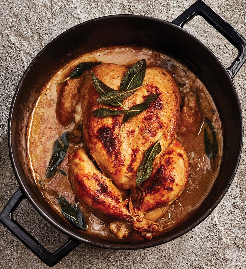A cast iron pot with a whole chicken covered in herbs and sauce