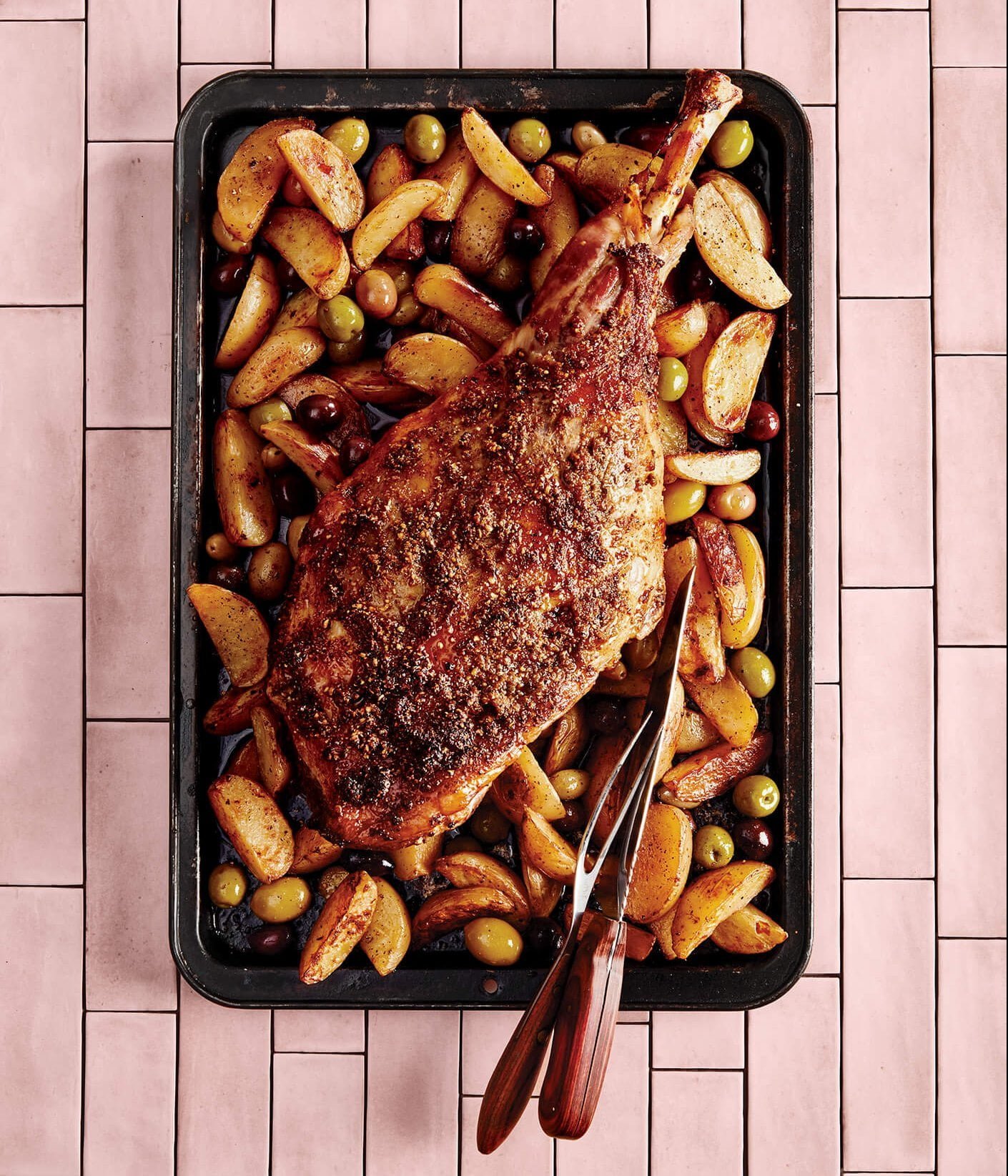 A pan with lamb and vegetables on a pink countertop