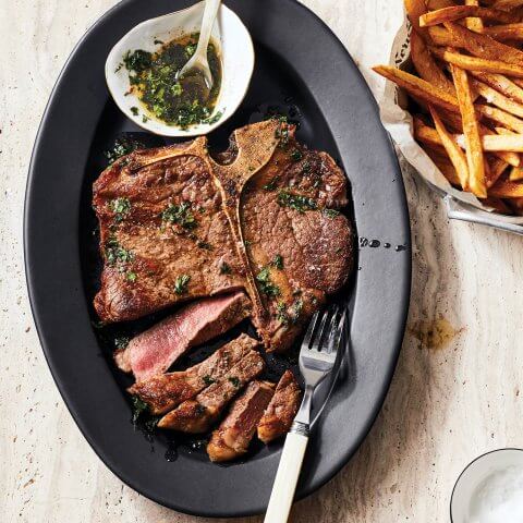 A sliced steak on a black plate with fries and sauce on the side.