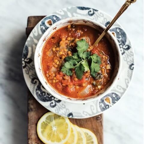 A bowl of easy vegetarian lentil soup with sliced lemons next to it