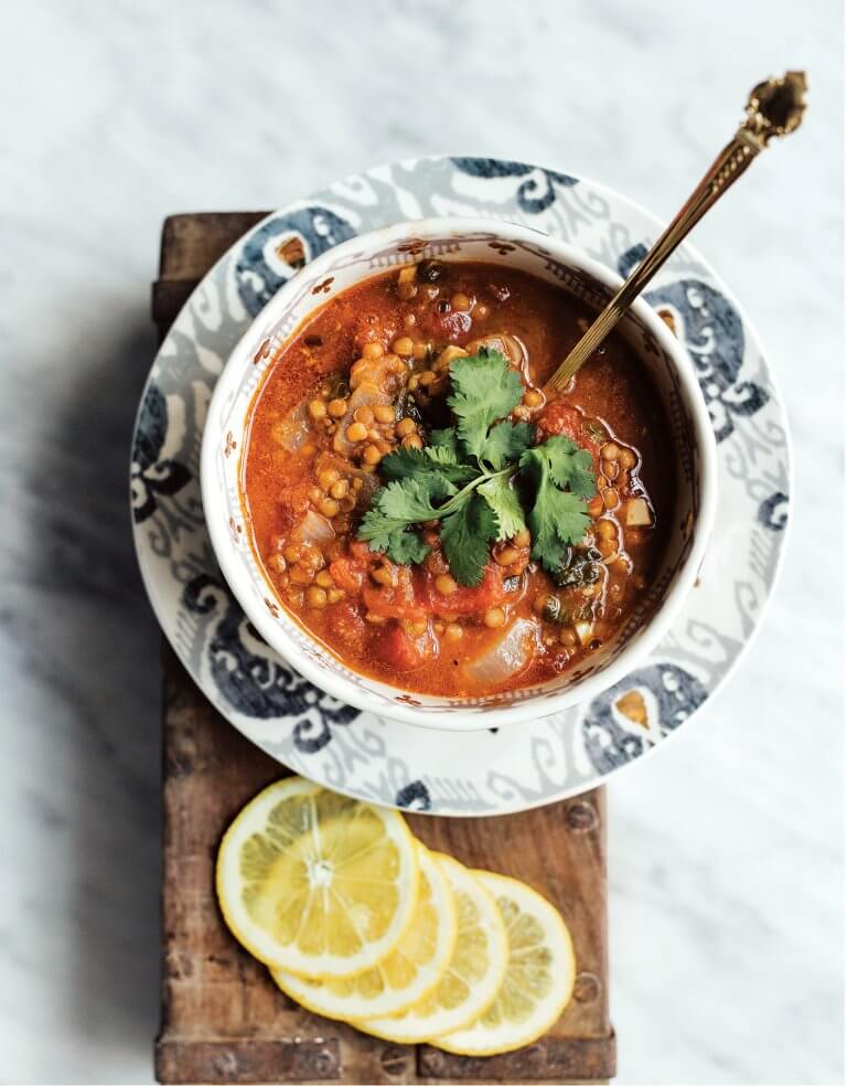 A bowl of easy vegetarian lentil soup with sliced lemons next to it