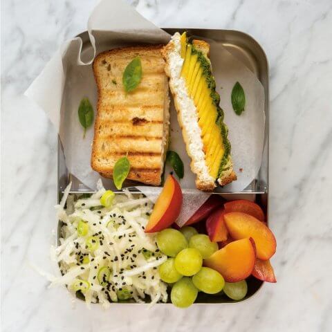 A sliced sandwich with fruit in a tin box