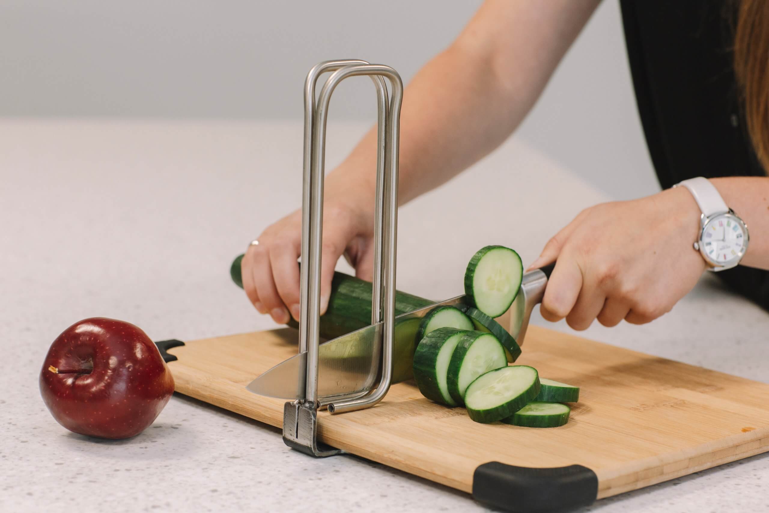 A person chops cucumbers with a metal tool attached to the cutting board.