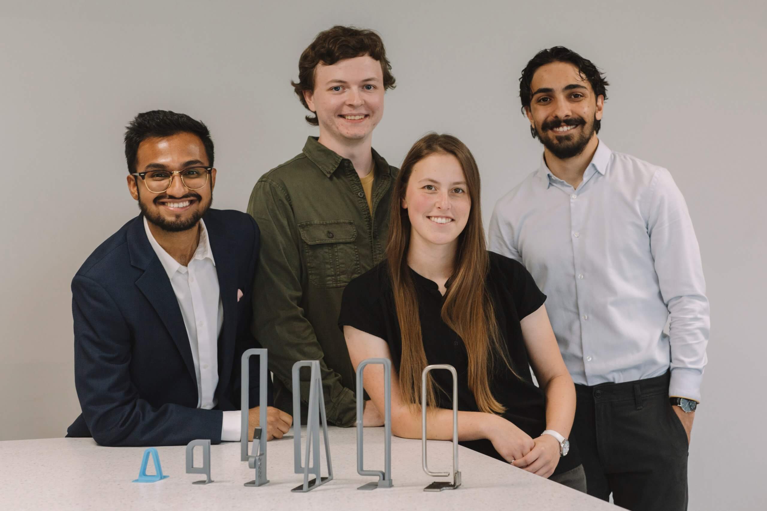 Four young people pose behind a line of metal devices.