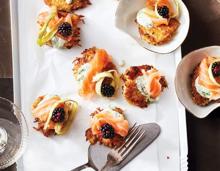 A white platter with bite-sized lox and latkes and cutlery