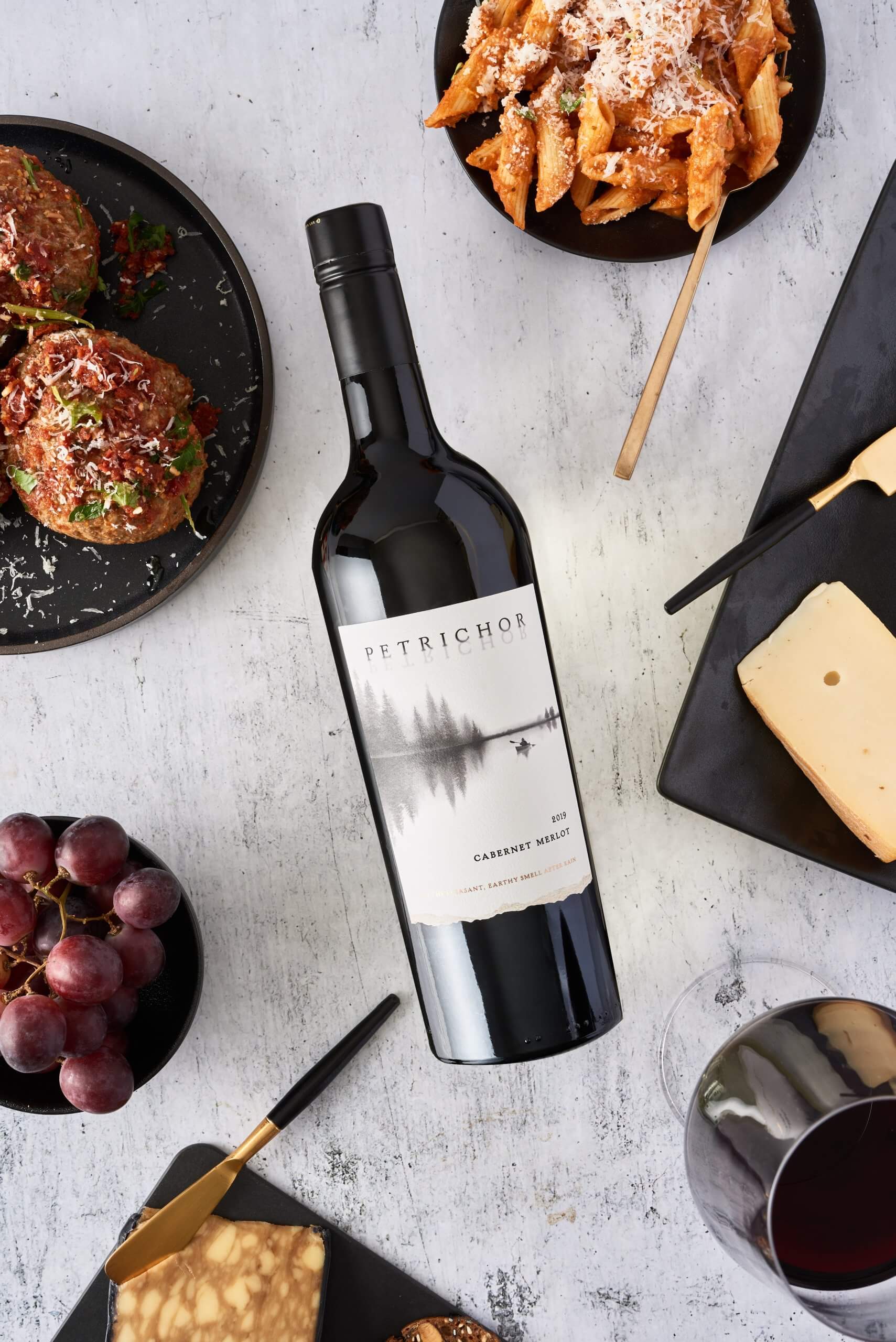 bottle of red wine on a marble table surrounded by food.