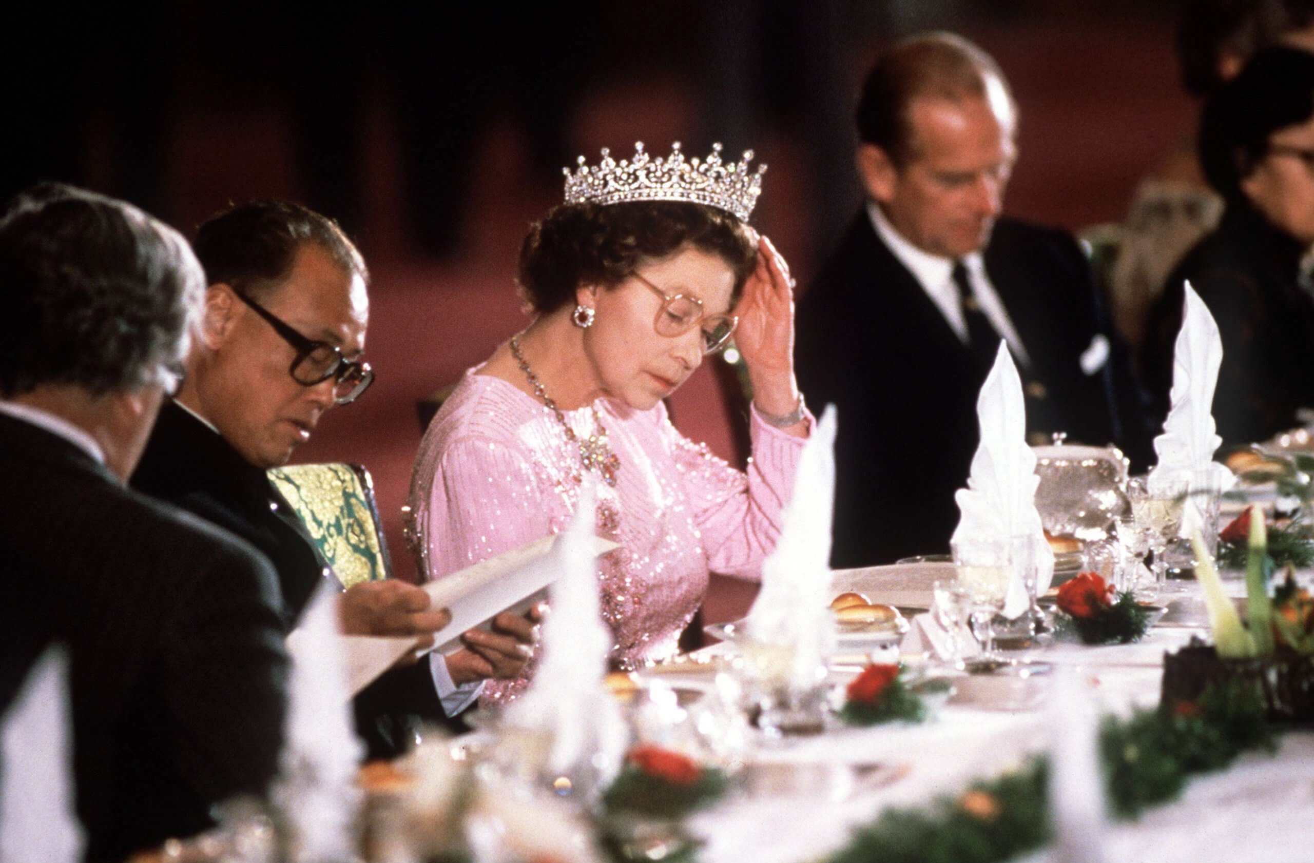 The queen adjusts her tiara at a banquet table