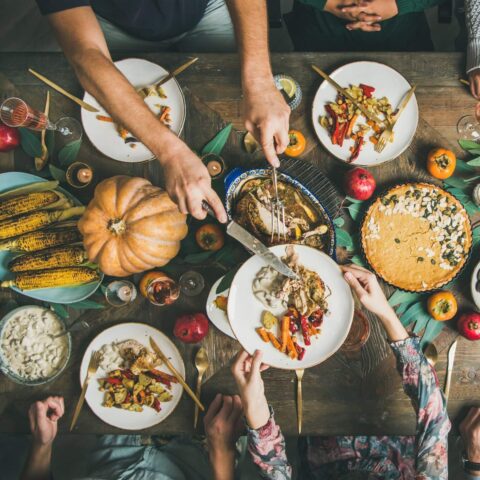 A wooden table topped with pie, pumpkins and plates of food.
