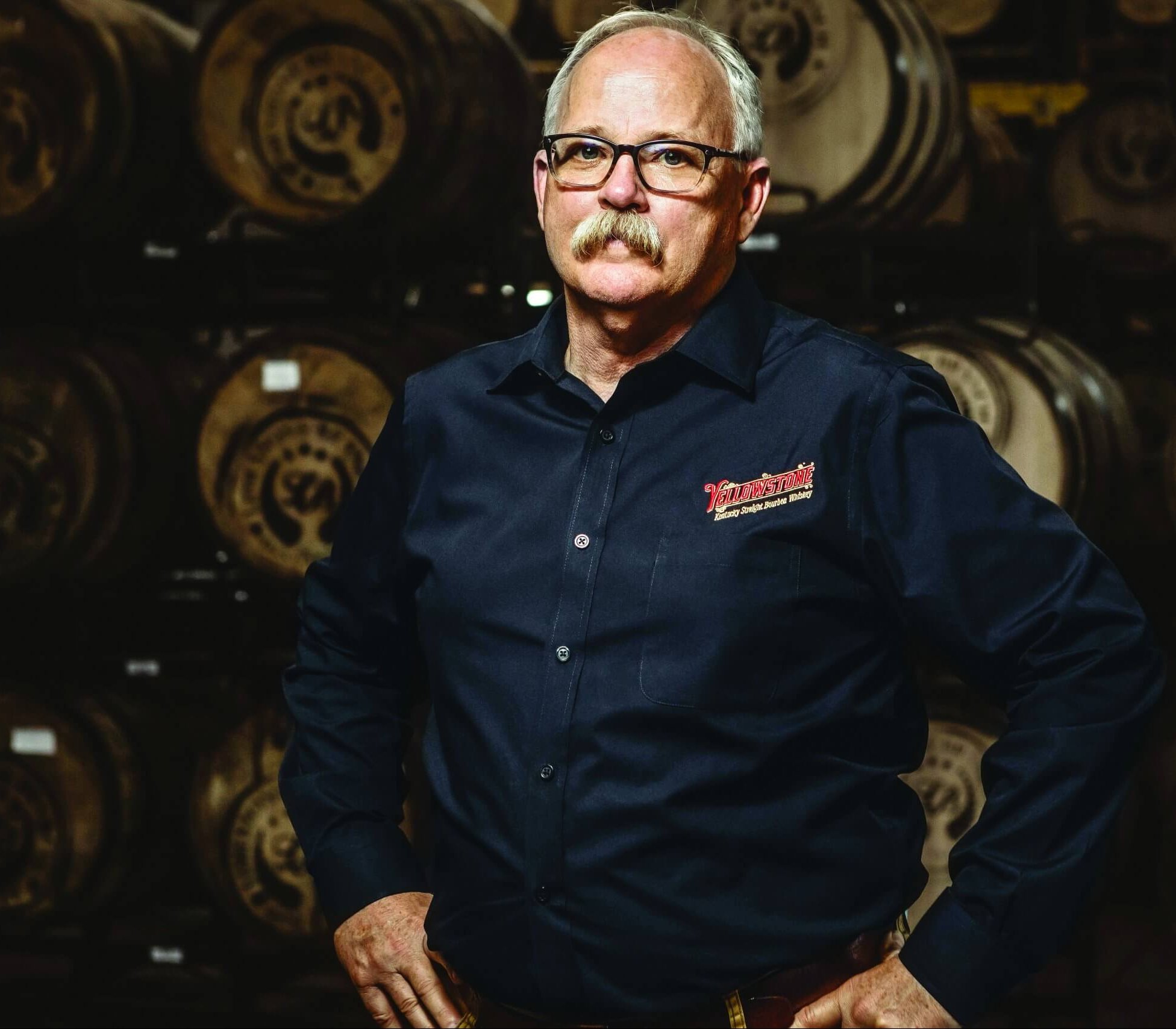 A man stands in front of a wall of barrels
