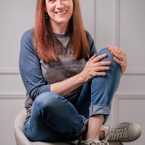A photo of Jennifer Emilson, A woman in jeans and a t-shirt sitting on a stool