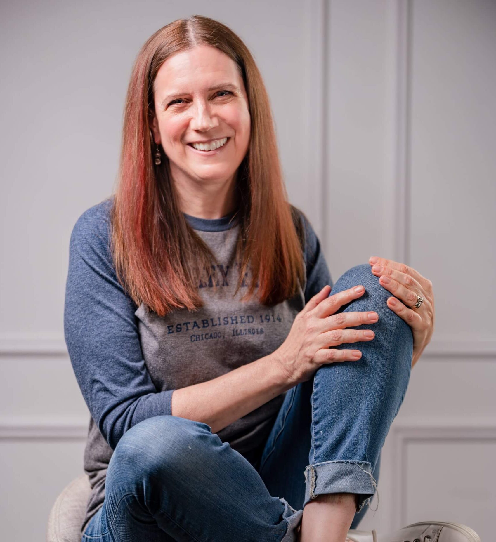 A photo of Jennifer Emilson, A woman in jeans and a t-shirt sitting on a stool