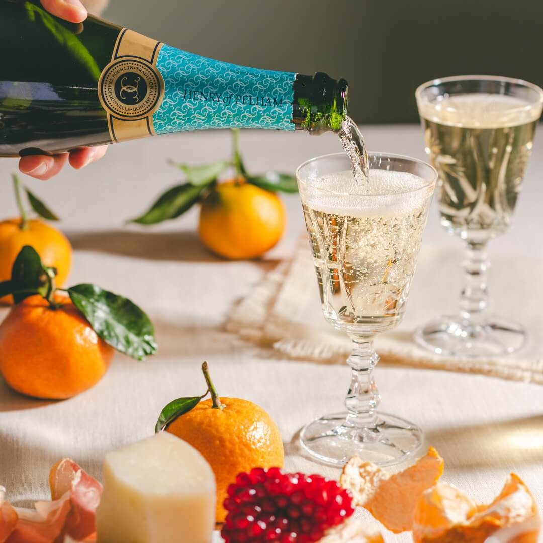 Henry of Pelham Cuvée Catharine Brut is being poured into a glass on a festive table with mandarin oranges.