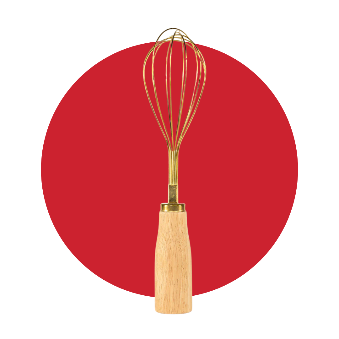 A gold standing whisk with wooden handle in front of a decorative red circle. 