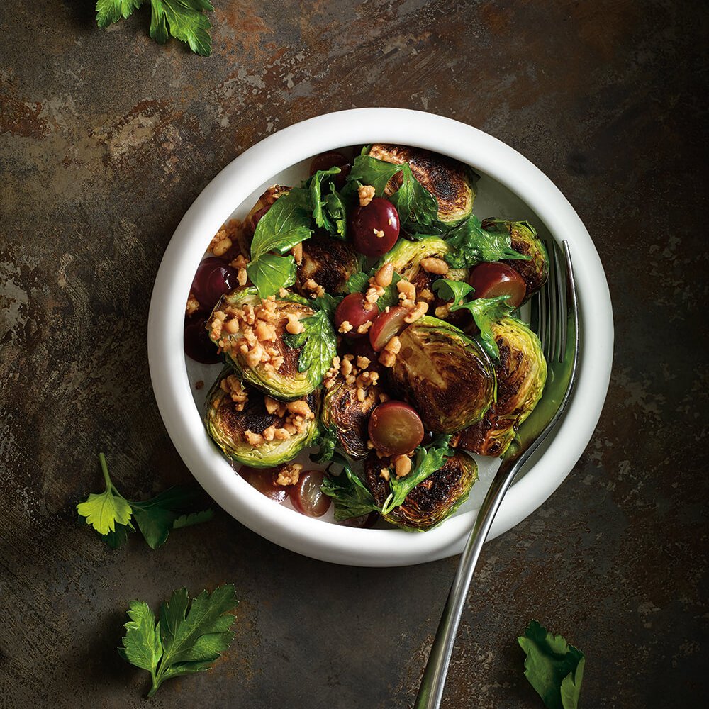 A white bowl with brussels sprouts and a serving spoon