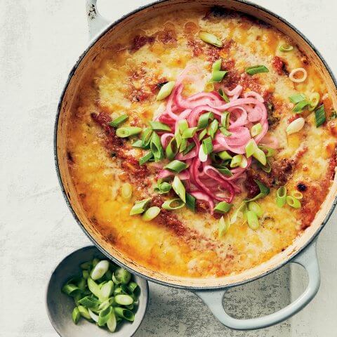 A pot with food and a side of green onikons shot from above.