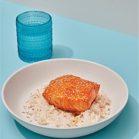 A dish with salmon on top of rice on a blue table with a blue glass.