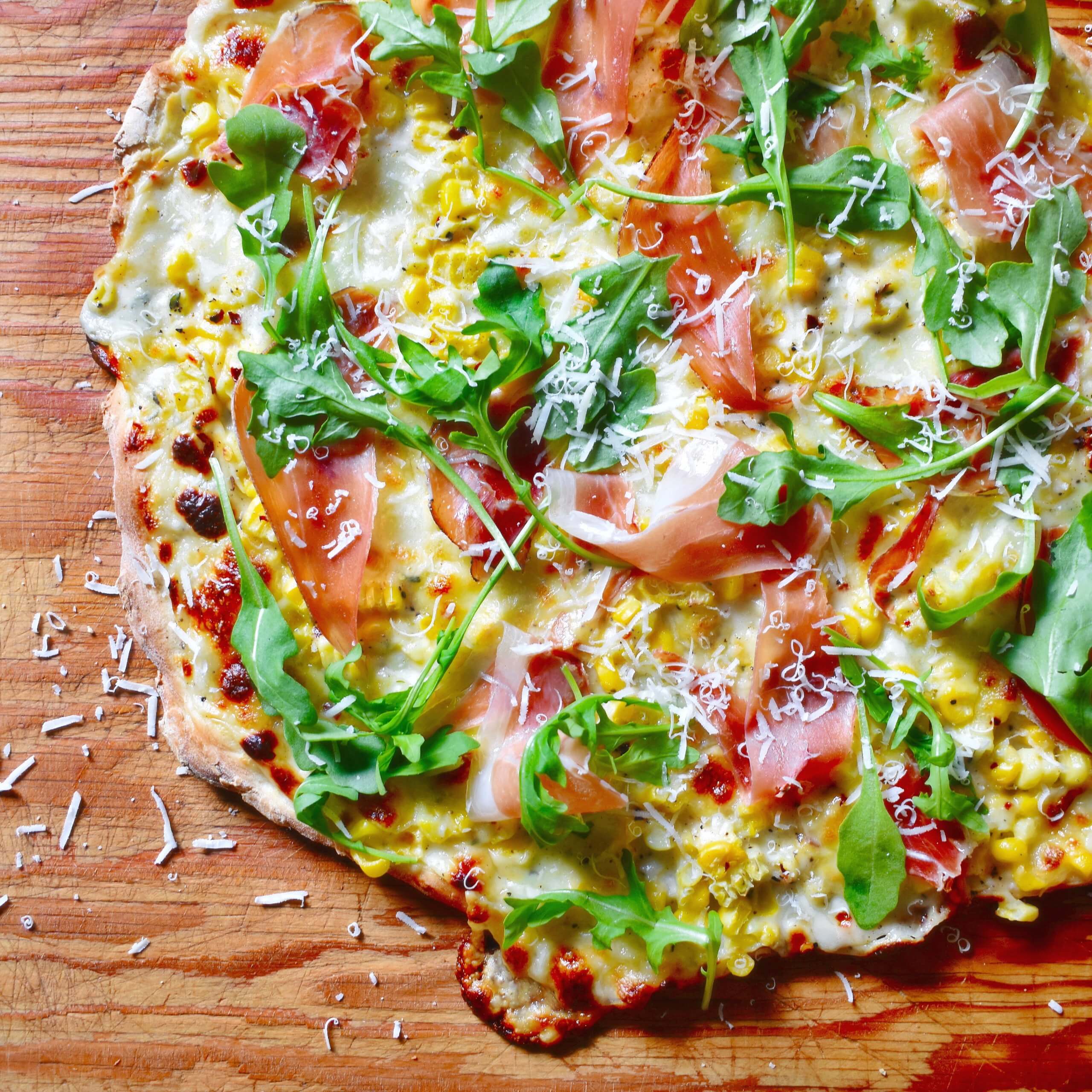 A pizza topped with arugula and tomatoes on a wooden board.