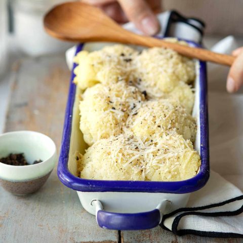A person holding a baking dish with cauliflower and cheese.