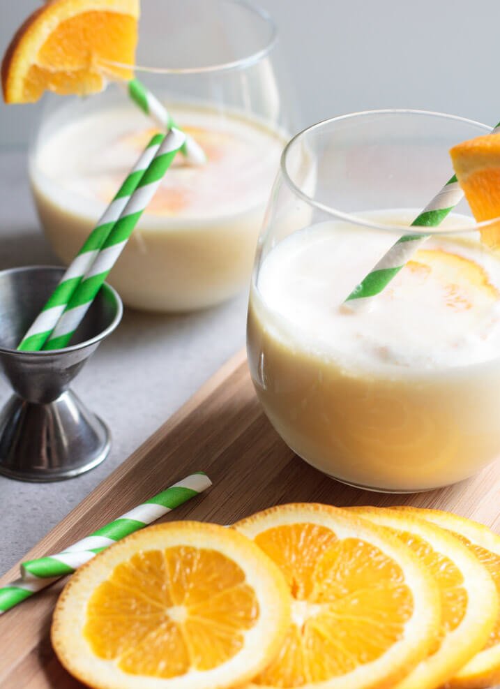 Sliced oranges next to glasses of a white cocktail with green-and-white straws.