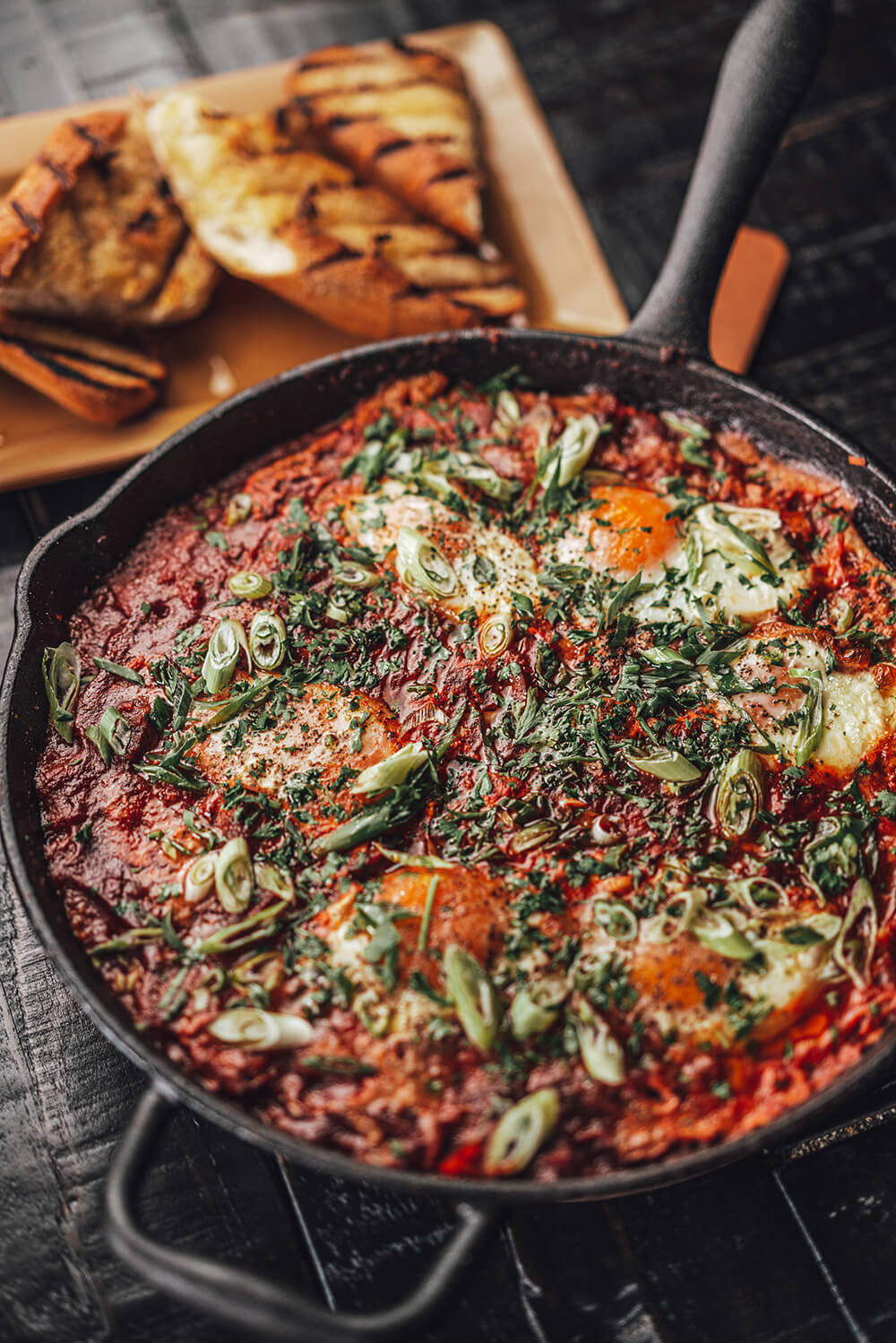 A skillet filled with shakshuka and sliced bread in the background.