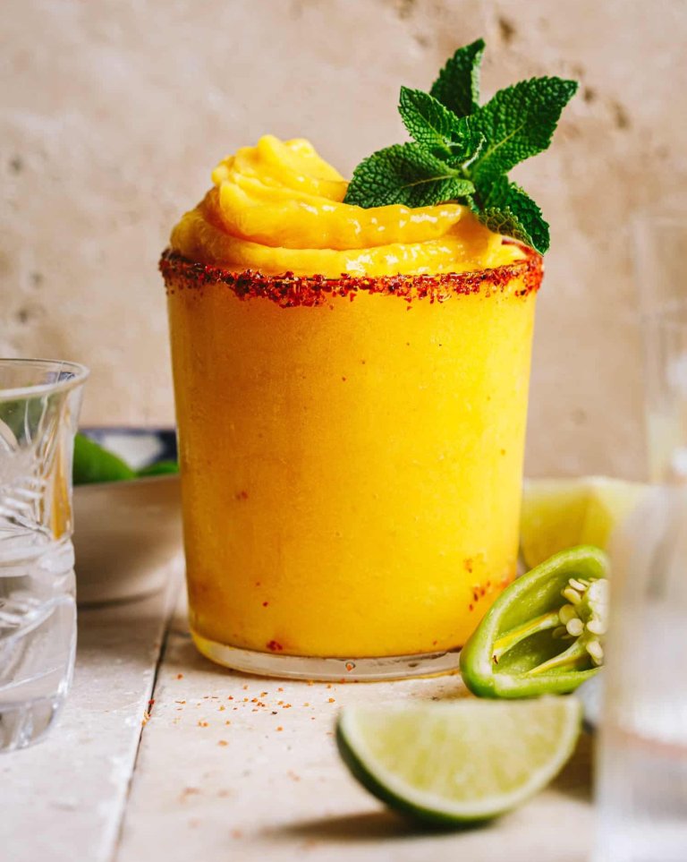 Frozen mango mezcal margarita in a glass with a salted rim on a wooden tabletop.