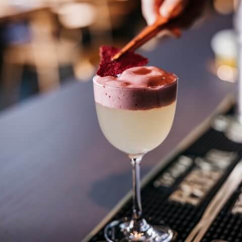 A closeup of a cocktail as a garnish is put on with tweezers.