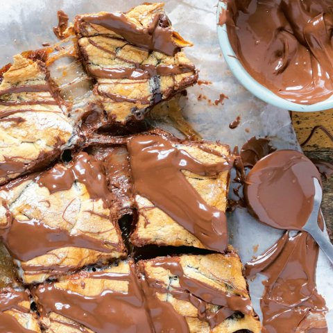 A tray of dessert bars with a bowl of chocolate next to it.