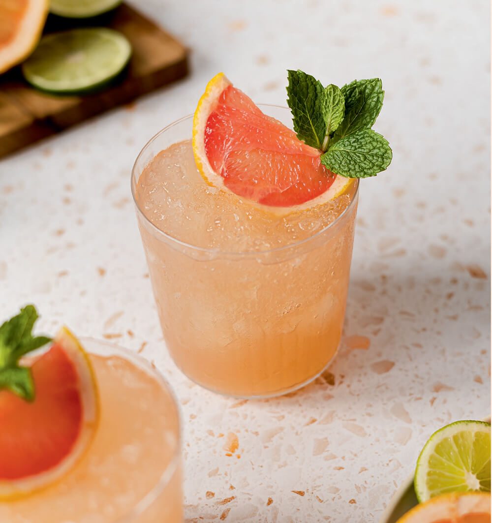 Glasses with a light pink drink and grapefruit garnish on a linoleum countertop.