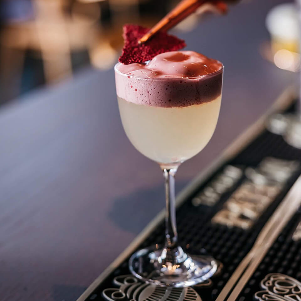 A cocktail being topped with a fruit leather garnish on a bar top