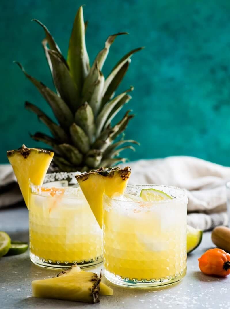 Cocktails garnished with pineapple in front of the fronds from one.