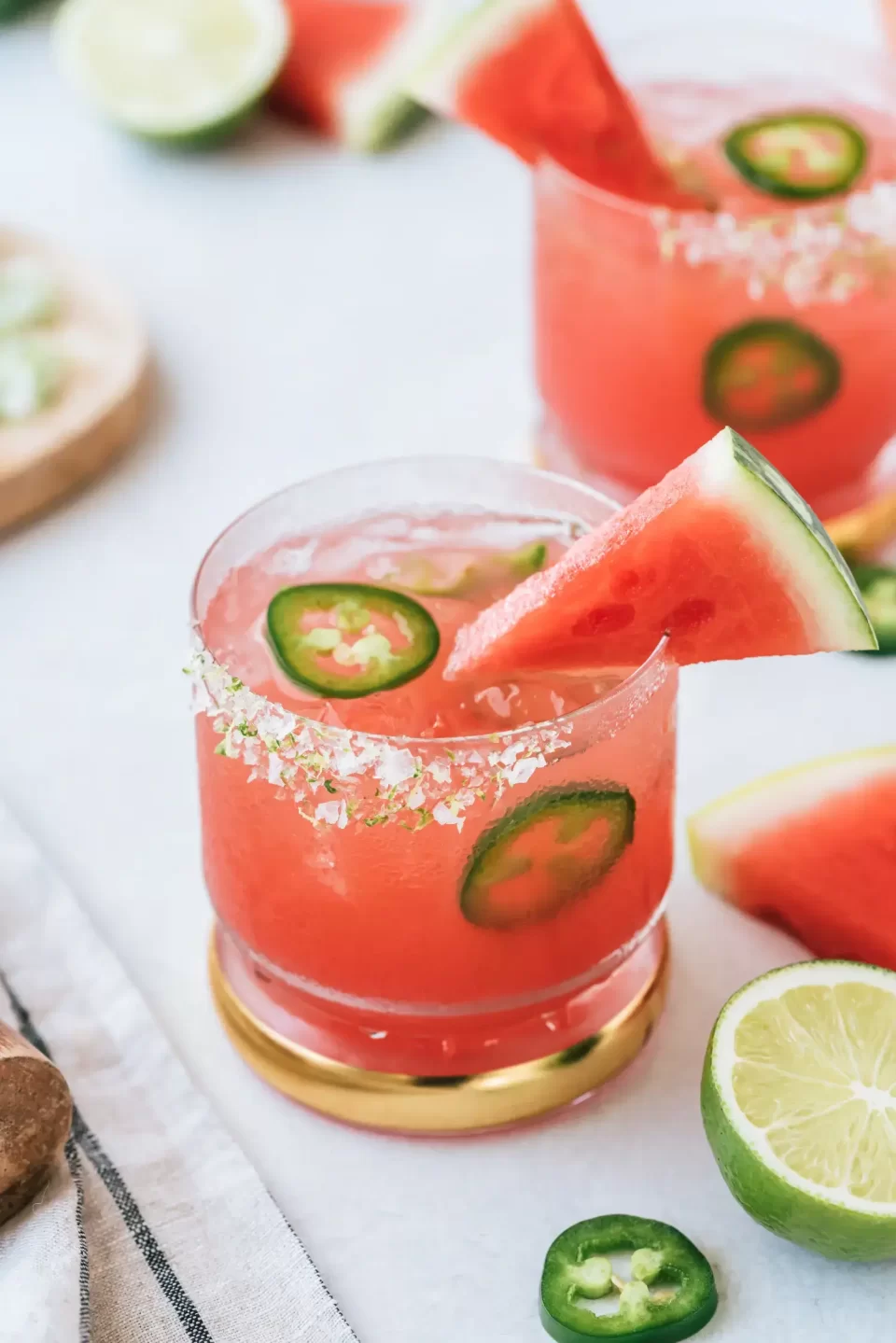 A pink cocktail jalapeños garnished with a slice of watermelon.