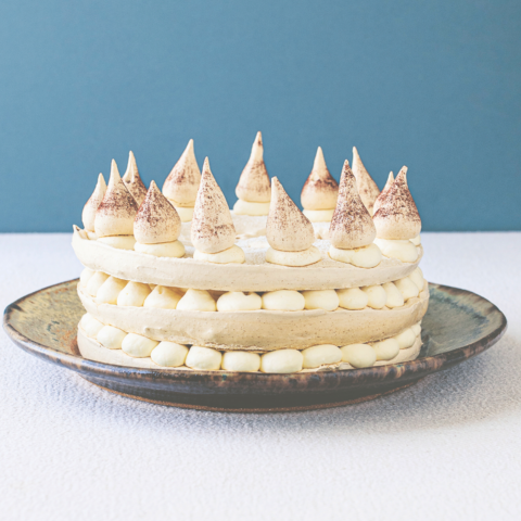An Irish Coffee meringue layer cake dessert on a plate with a blue wall in the background.