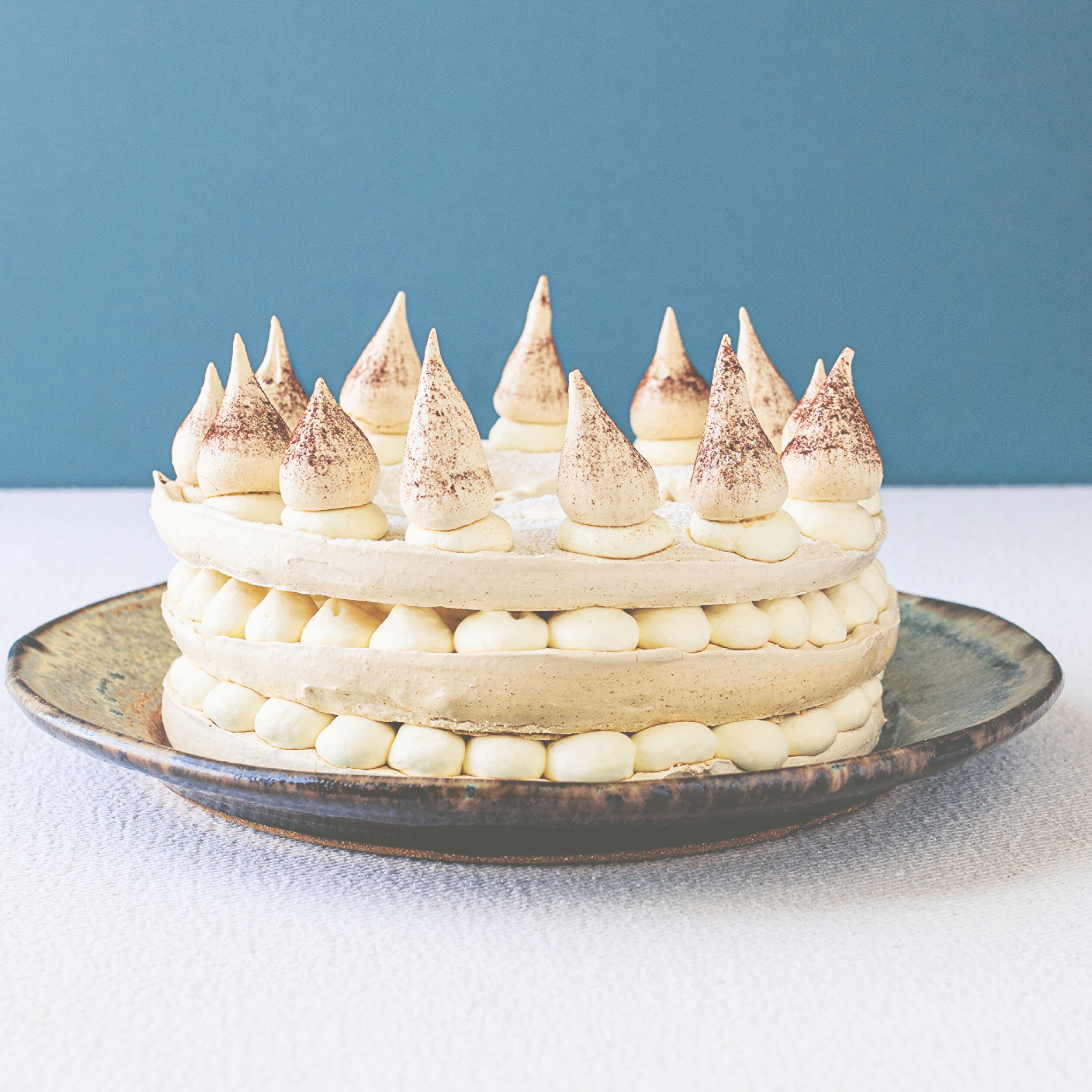 An Irish Coffee meringue layer cake dessert on a plate with a blue wall in the background.