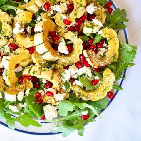 A closeup shot of a salad with roasted squash in a clear glass bowl from above.