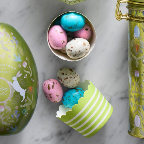 Two green paper cartons filled with pink, blue and white speckled chocolate eggs on a marble countertop.