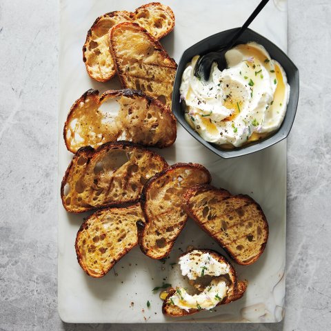 A stone surface with grilled crostini and a recipe for whipped chive ricotta with truffle honey
