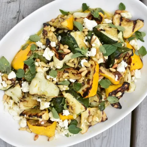 A white platter with salad on a grey wooden table.