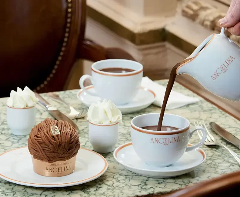 A light green table with desserts and hot chocolate being poured into a white mug.