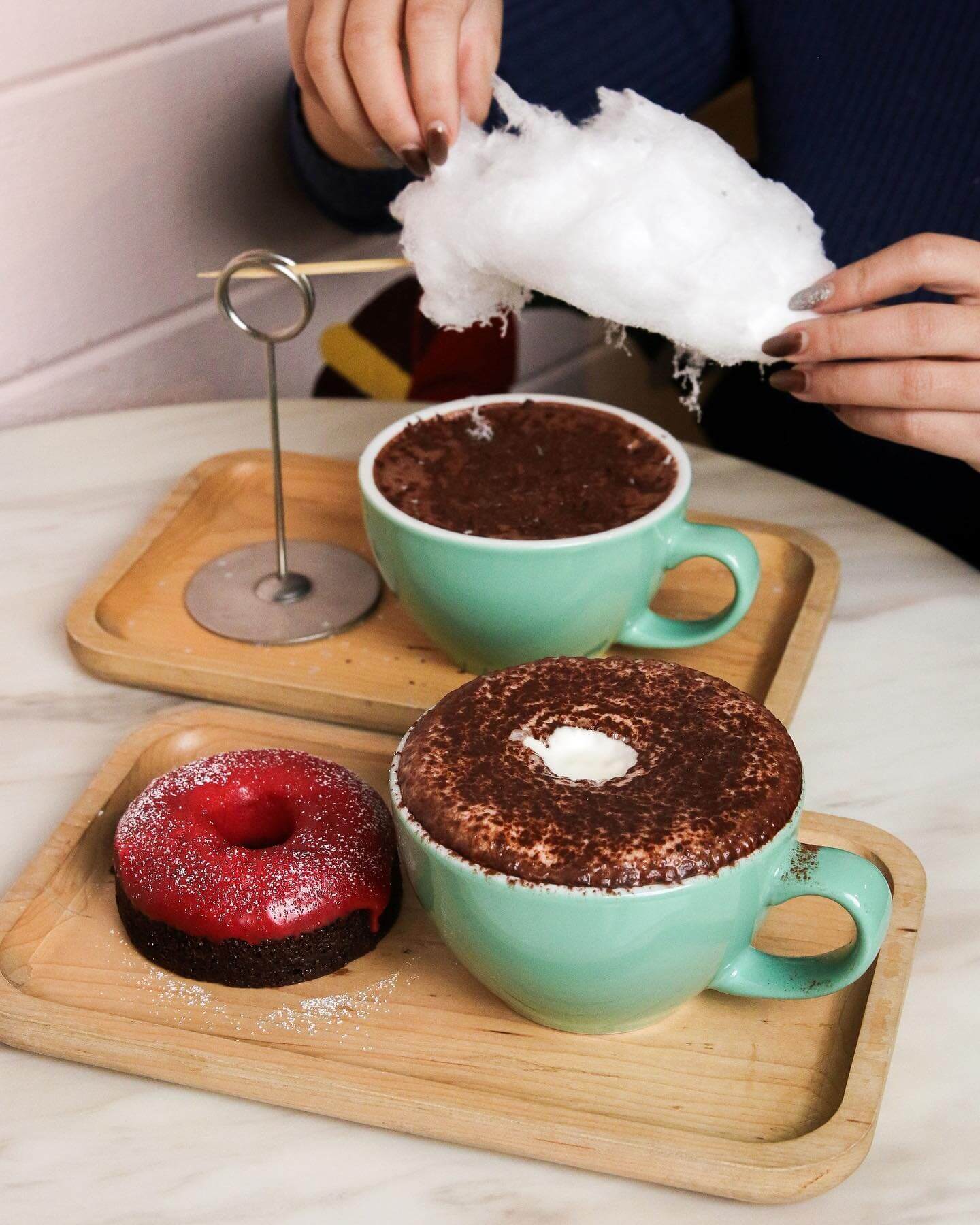 Two wooden trays with turquiose mugs of hot chocolate, a red donut and cotton candy cloud.