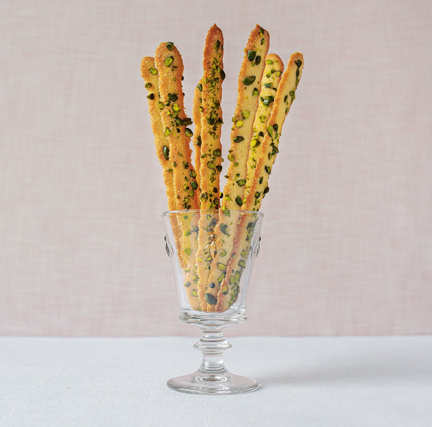 A glass with biscuits photographed on a white surface with a light pink wall in the background